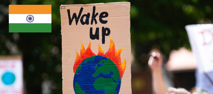A protester holding a sign of a burning earth saying 'wake up', featuring the Indian flag.